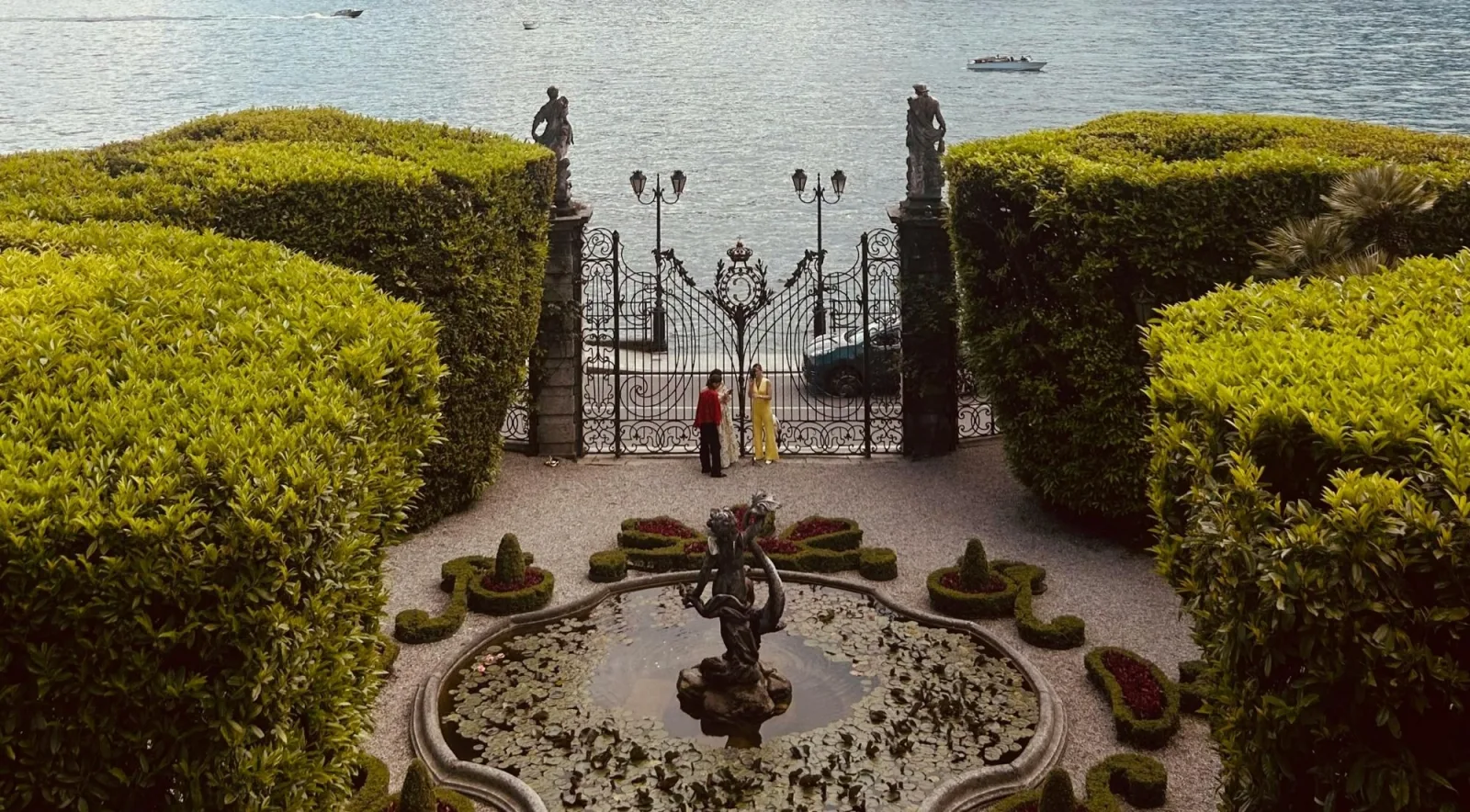 The formal garden, statues and lakeside gate of a historic Lake Como villa seen from above