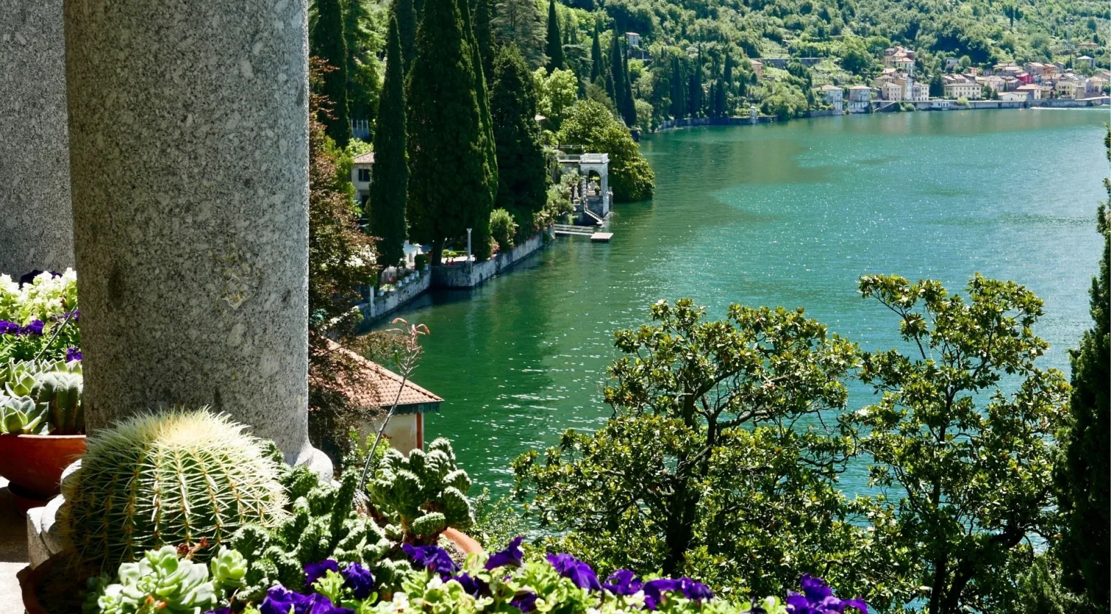 A villa garden overlooking the emerald water of Lake Como toward a distant village