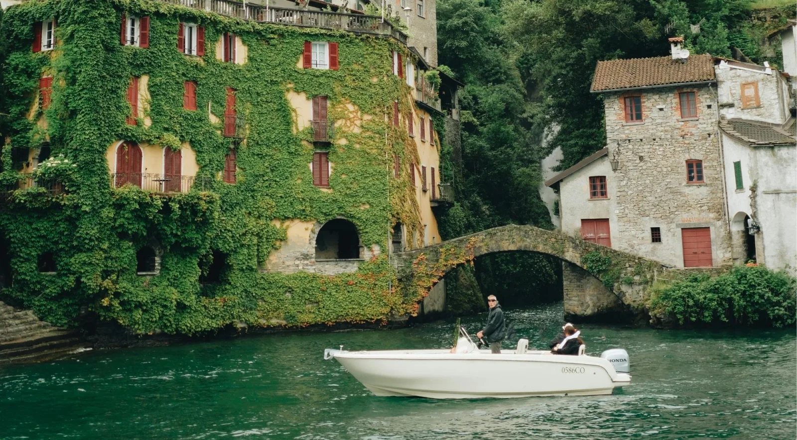 The stone bridge and ivy-clad house of Nesso village with a small boat on Lake Como
